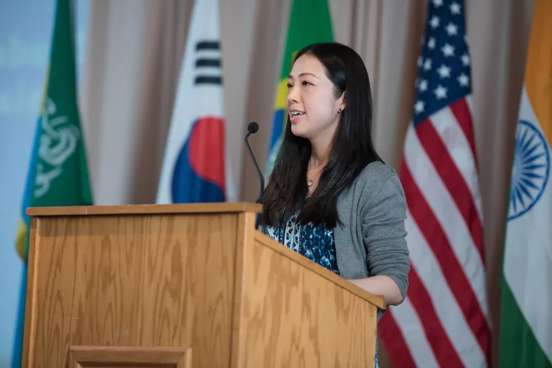 International student speaking at podium with flags from various countries in background